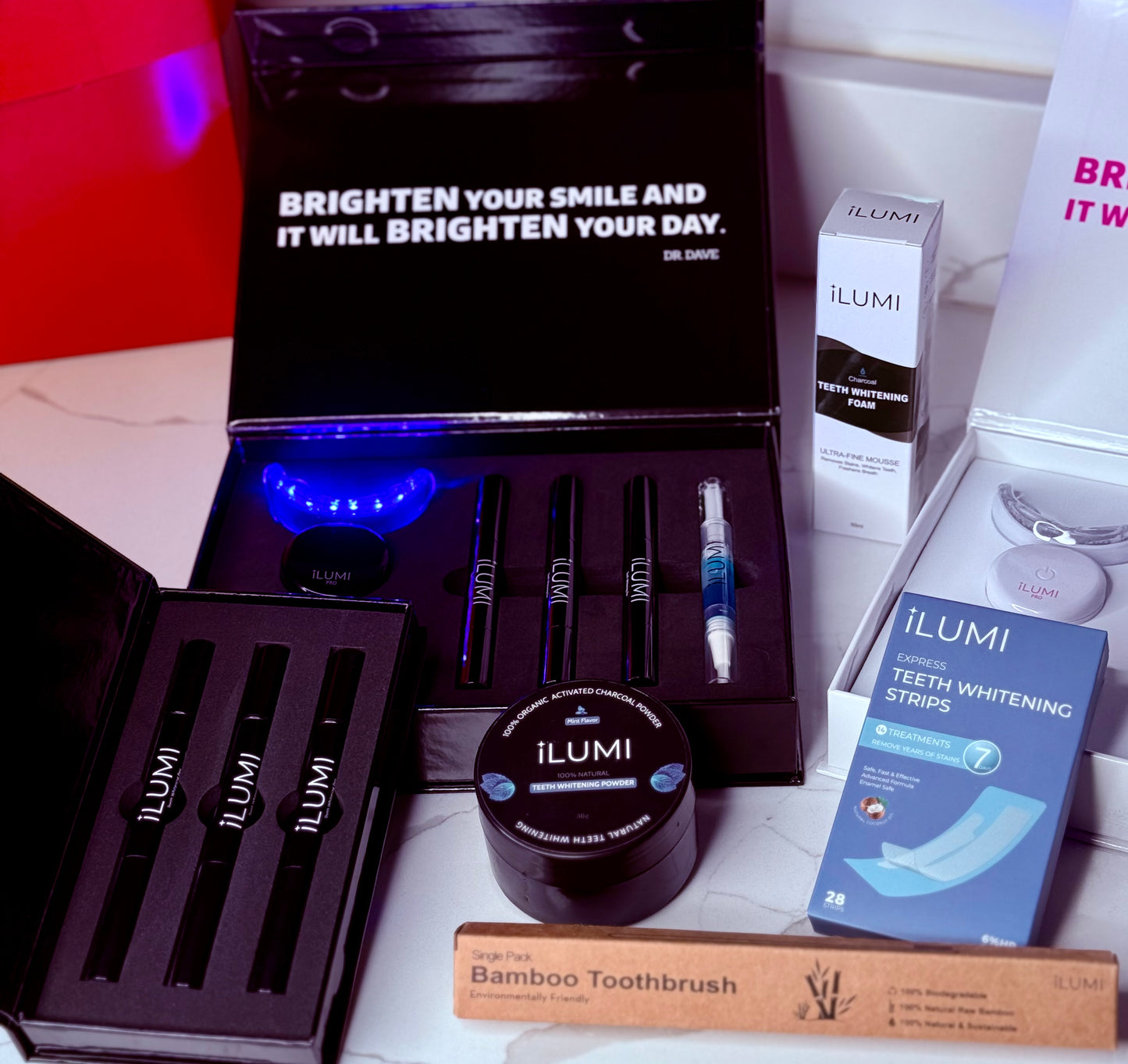Ilumi teeth whitening products including strips, light, and bamboo toothbrush on a white surface.